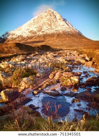 Sunny winter day on meadow at river Coupall at delta to river Etive. Snowy cone of mountain Stob Dearg 1021 metres high. Higland in Scotland an marvelous day. Dry grass and heather bushes on banks. 