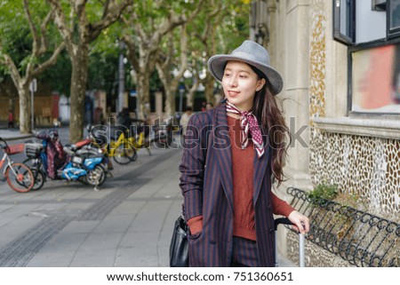 Beautiful Chinese woman in suit stand at the corner of street with suitcase beside her.