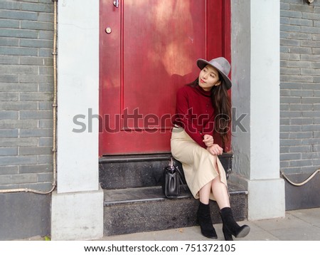 Beautiful Chinese sit on the step in front of a red door, waiting someone to go home.