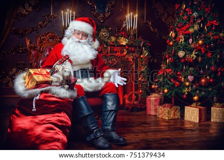 Surprised Santa Claus in a beautiful room next to the fireplace and Christmas tree sits with a sack of gifts .  Royalty-Free Stock Photo #751379434