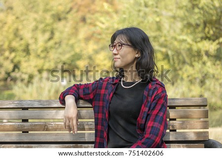 An Asian woman sitting on a chair in the park, wearing glasses