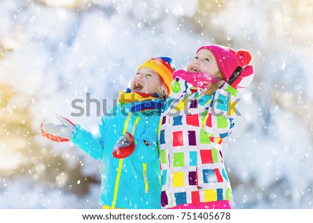 Kids playing in snow. Children play outdoors on snowy winter day. Boy and girl catching snowflakes in snowfall storm. Brother and sister throwing snow balls. Family Christmas vacation activity.