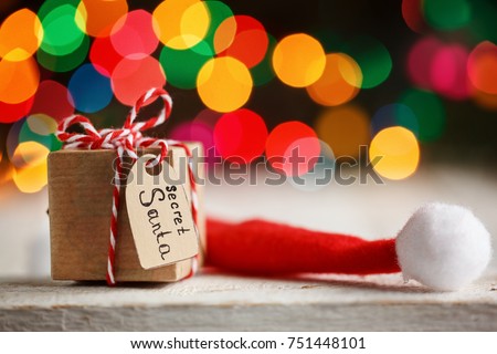 Christmas present or box for secret santa with Santa hat on colorful bokeh background.