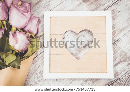 Rustic styled purple roses bouquet over wooden table with wood frame with heart. Top view. 
