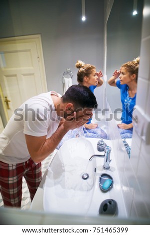 Young attractive couple preparing their faces in the bathroom for a new day in the morning while standing in pajamas.