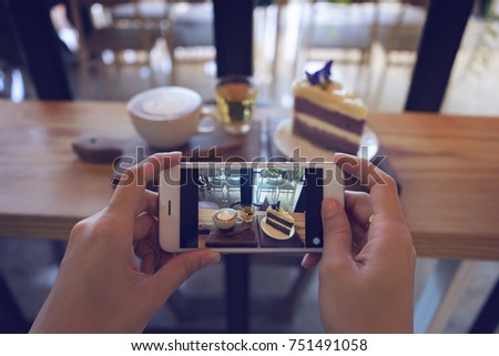 Close-up hand holding phone taking coffee and cake photo on table. People using smartphone take a photo in coffee shop. 