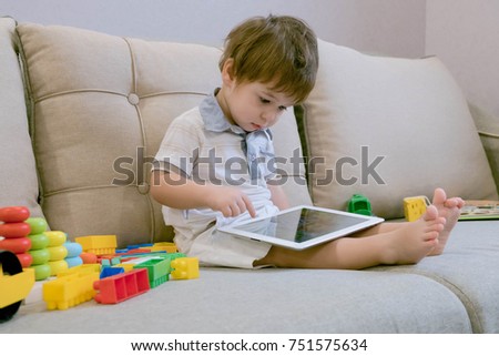 Toddler boy playing with digital tablet on couch at home