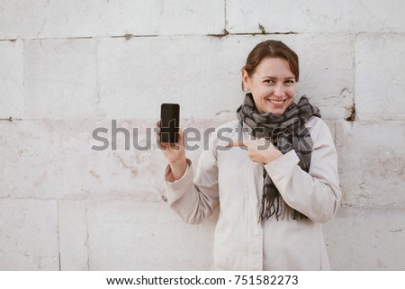 A woman in scarf is smiling and pointing on her phone