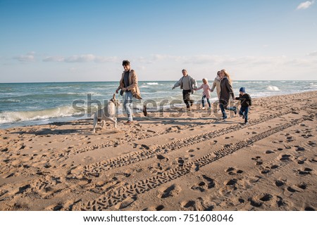 big multigenerational family running with labrador dog on beach at seaside Royalty-Free Stock Photo #751608046