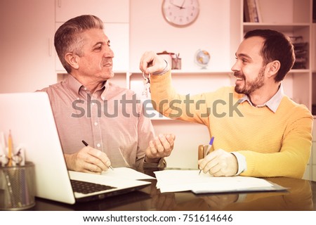 Mature man and young agent sign rental agreement in agency and hand over keys