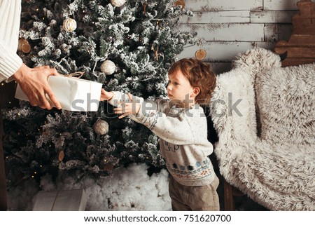 Happy father gives a Christmas gift to his son in decorations with fir tree with gift boxes and wooden background.