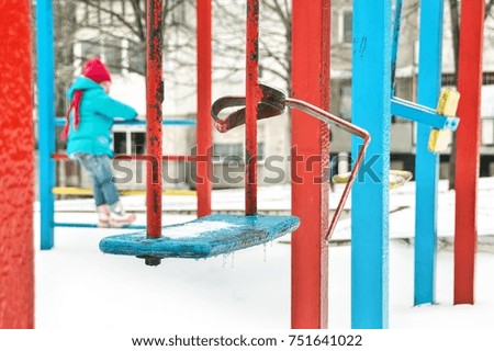 Snow and ice on the colorful children playground in the park. Abstract vertical red and blue pattern. Shallow depth of focus. Winter play and activity concept. 