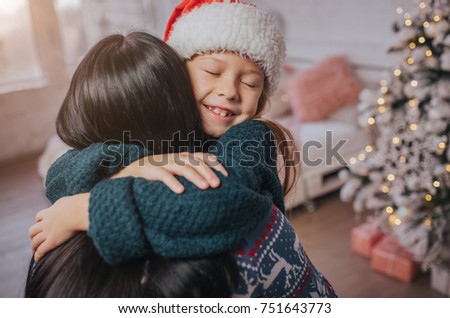 Merry Christmas and Happy Holidays! Cheerful mom and her cute daughter girl exchanging gifts. Parent and little child having fun near Christmas tree indoors. Morning Xmas. Portrait family close up.