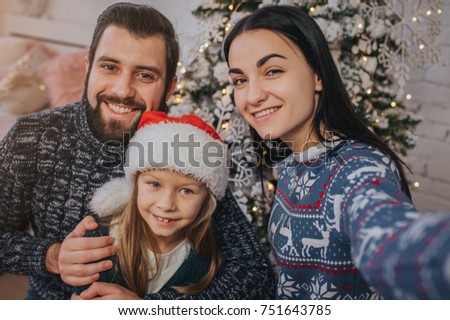 Smiling young family in Christmas atmosphere making photo with smartphone.