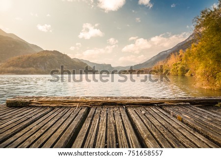 beautiful view of Cavazzo lake from wooden wharfboat against mountains and blue cloudy sky background in Friuli Venezia Giulia, Italy