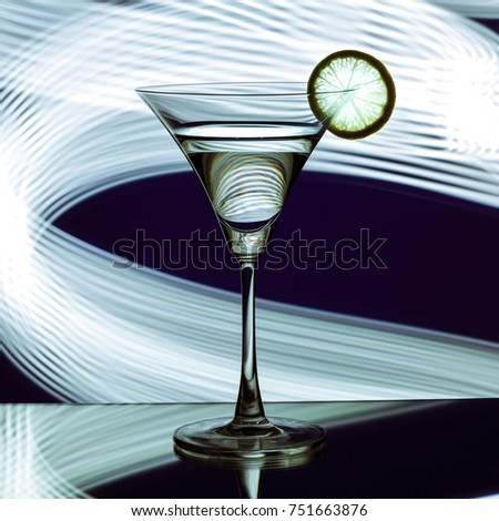 silhouette of a glass with cocktail and lemon on background of fantasy stripes of light