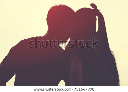 Closeup silhouette of beautiful couple on orange sky. Sun between lips of two young people in love