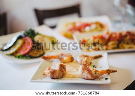 Bacon Shrimp, fried calamari and antipasto appetizer sitting on table with white table cloth in fine dining restaurant with window light. Film grain look