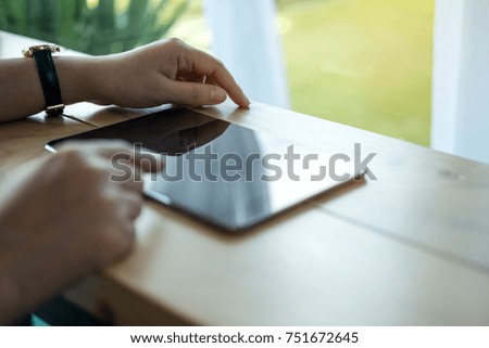 Closeup image of a woman's hands pointing , touching and using tablet pc  on wooden table in cafe