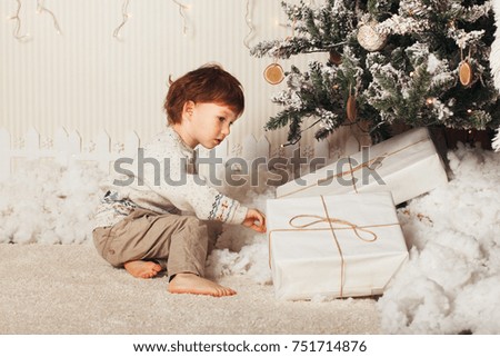 Cute little boy is sitting with a gift near the Christmas tree. The child is happy with New Year's gift.