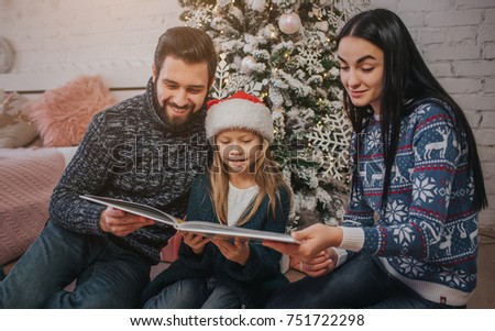 Merry Christmas and Happy Holidays! Cheerful mom, dad and her cute daughter girl exchanging gifts. Parent and little child having fun near Christmas tree indoors Morning Xmas. Portrait family close u