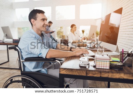 Disabled person in the wheelchair works in the office at the computer. He is smiling and passionate about the workflow. Royalty-Free Stock Photo #751728571