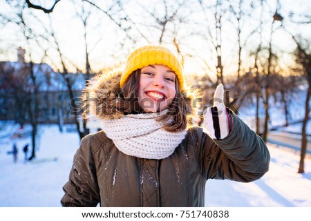 Hipster crazy girl with surprise expression in yellow cup heaving fun in winter park in snowy sunny winter day. Woman balancing and wave with her arms wth coloful mittens. Pictures in warm colors.