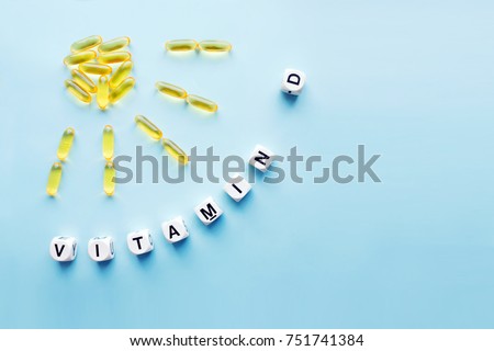 Yellow capsules in the form of the sun with rays and word vitamin D from white cubes with letters on blue background. VITAMIN D word for healthy and medical concept. Sunshine vitamin health benefits Royalty-Free Stock Photo #751741384