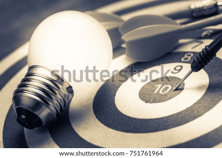 Dart hit on the center of dartboard with glowing light bulb