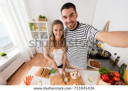 technology, people and eating concept - happy couple cooking food and taking selfie at home kitchen