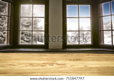 A table with space for your product decoration or advertising slogan. Great old window overlooking the mountains and a forest full of snow. Beautiful cloudy sky on a sunny day.