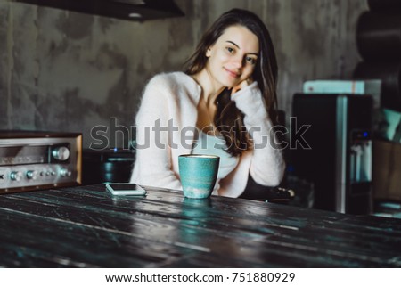 a beautiful brunette girl with a charming smile and expressive brown eyes drinking coffee and using a smartphone, checking social networks, doing photo selfi