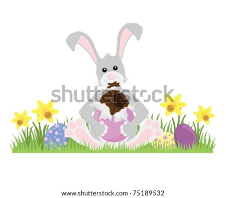 Grey Easter Bunny sitting on grass eating a large chocolate Easter Egg, isolated on white.