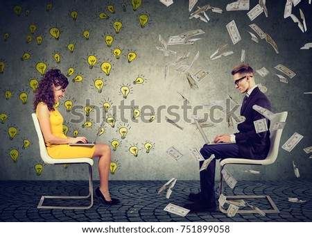 Serious businessman and businesswoman working on laptop computer one under money rain another under bright ideas light bulbs
