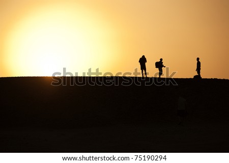 Three people in the desert silhouetted against an orange sunset