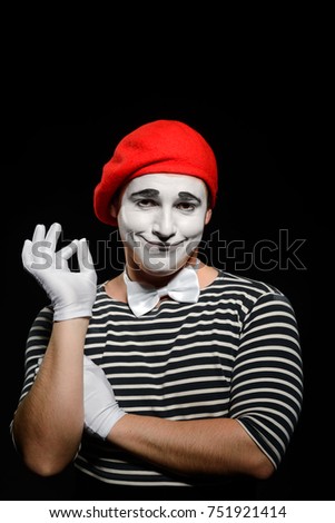 Portrait of smiling male mime on black. Man wearing striped t-shirt, red beret, white gloves and bow tie and performing a dumb show.