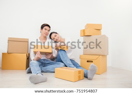 Asian woman and asian man carry boxes sitting on the floor with pile of boxes. Moving house just married asian couple concept. 