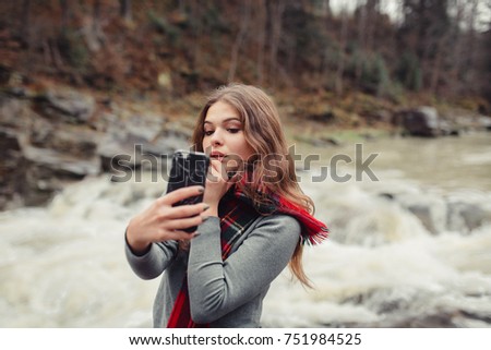 A young stylish brunette hipster woman in nature, taking selfie with her smartphone. Girl with mobile phone take a picture of herself