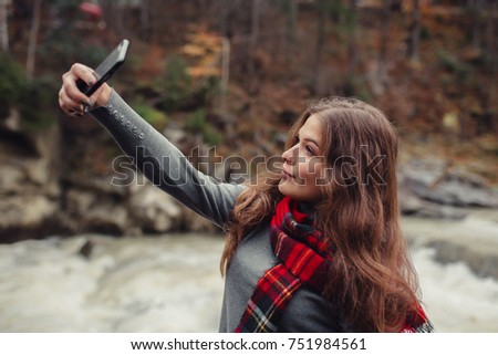 A young stylish brunette hipster woman in nature, taking selfie with her smartphone. Girl with mobile phone take a picture of herself