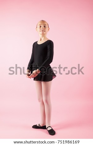 Portrait of young beautiful child girl ballerina standing practicing ballet wearing black tutu dress posing in studio with light pink background. Copy space image.
