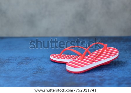 Red striped sandals lay on blue wooden floor.