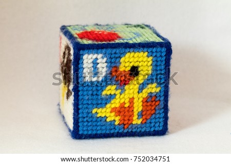 Child's needlepoint alphabet block. Letter D with duck image. White background.