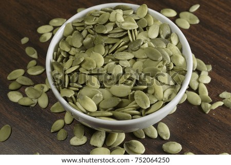 Vegan food. Raw pumpkin seeds for roasting in a white dish. Wooden background.