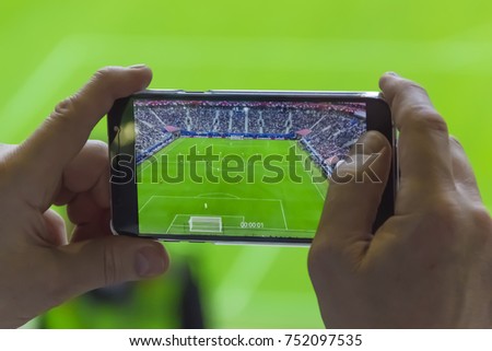 Selective focus on hands using mobile phone taking picture of football match