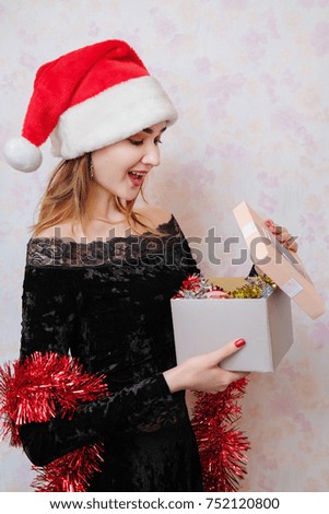 The women in a black dress and red tinsel having fun, smiling and throwing confetti and glitter, celebrates New Year 2018, Christmas. Girl in red santa claus hat open a gift.
