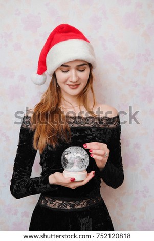 The women in a black dress and red tinsel having fun, smiling and throwing confetti and glitter, celebrates New Year 2018, Christmas. Girl in red santa claus hold a magic snowy ball.
