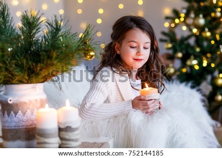 A brunette gilr in front of fur-tree and fireplace with candles and gifts. A surprised girl. A girl dreaming. New year's eve. Christmas eve. Cozy holiday at the fur-tree with lights and gold decor.