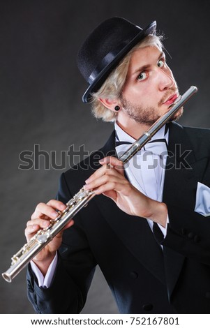 Classical music, passion and hobby concept. Elegantly dressed musician man playing on flute wearing black fedora hat. Studio shot on dark grey background