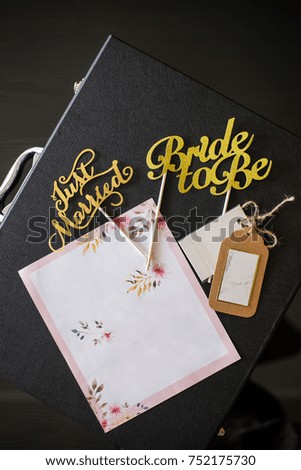 just married and bride to be sticks with designed paper card and tags on top of a black leather suitcase