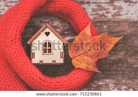  toy house is wrapped in a warm scarf with an autumn leaf. The concept is warm, cozy, loving, protecting the house. We prepare the house for the cold. Royalty-Free Stock Photo #752230861